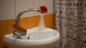 A white sink with a chrome faucet, a red flower in a white vase, and a wall with Hebrew letters. - Smart Apartment Filatova 10a (Lviv)