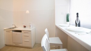 A modern kitchen with white cabinetry, a sink, a small refrigerator, and a window with blinds. - Smart Apartment Filatova 10a (Lviv)