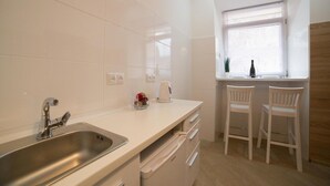 A modern kitchen with a stainless steel sink, white cabinets, and two white bar stools. - Smart Apartment Filatova 10a (Lviv)