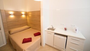 A compact hotel room with a bed, a small kitchenette, and a white tiled wall. - Smart Apartment Filatova 10a (Lviv)