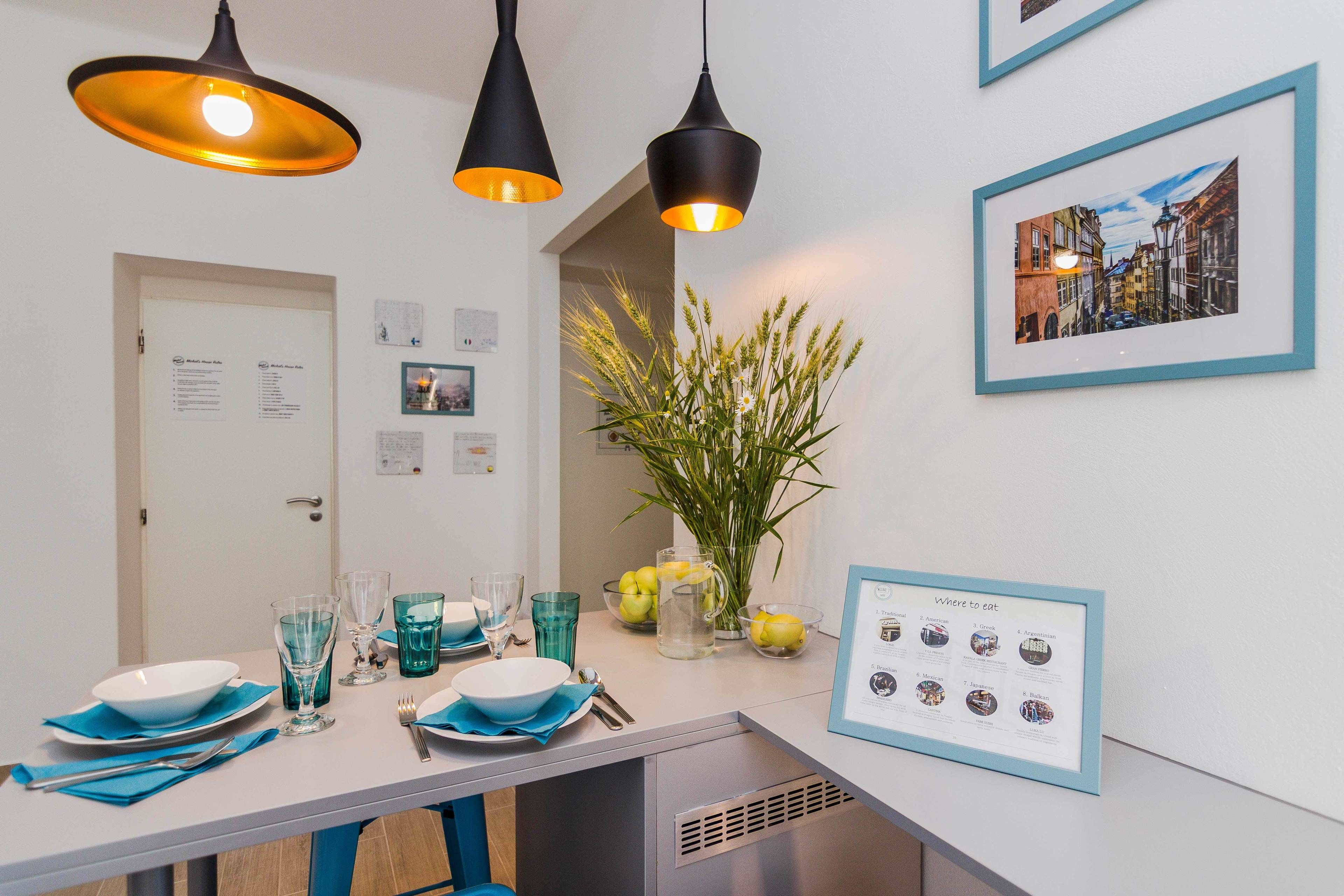 Un coin repas avec une table dressée pour quatre personnes, deux lampes suspendues, un tableau encadré et un menu affiché au mur.