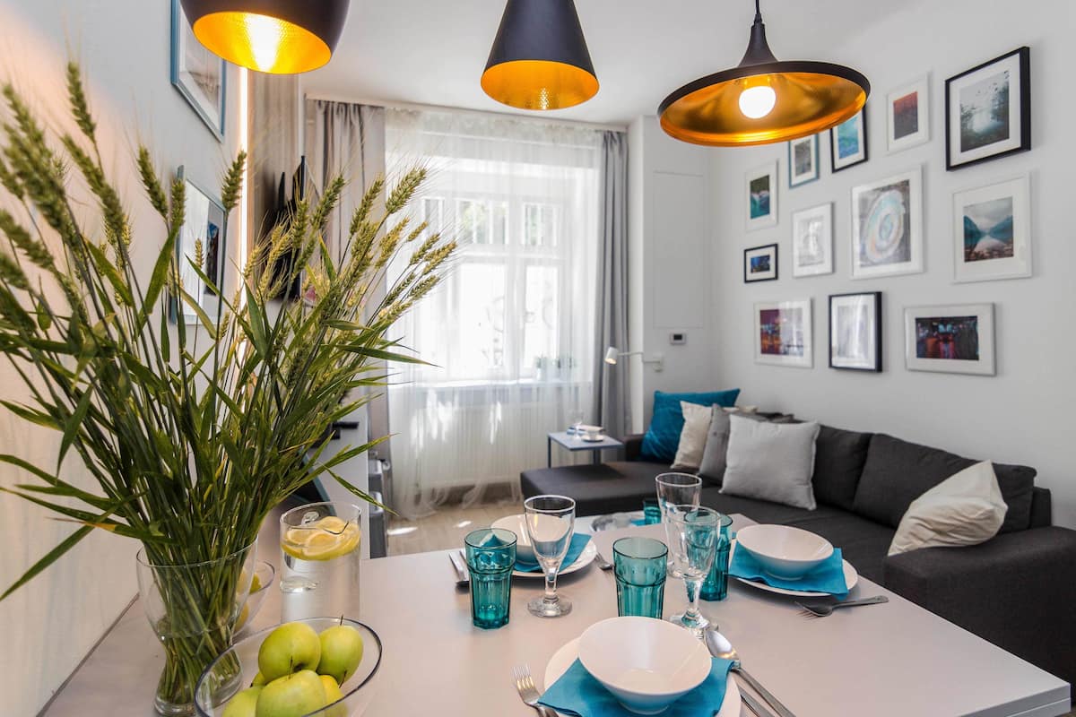 Een moderne eethoek met een tafel gedekt voor vier personen, een vaas met groene planten en uitzicht op een balkon met een deur en gordijnen.