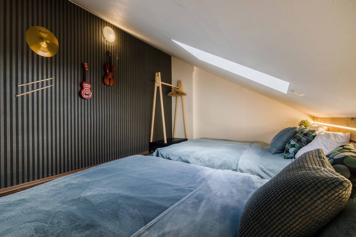 Een slaapkamer met een schuine kap, een dakraam, een trommel, een viool en een standaard.