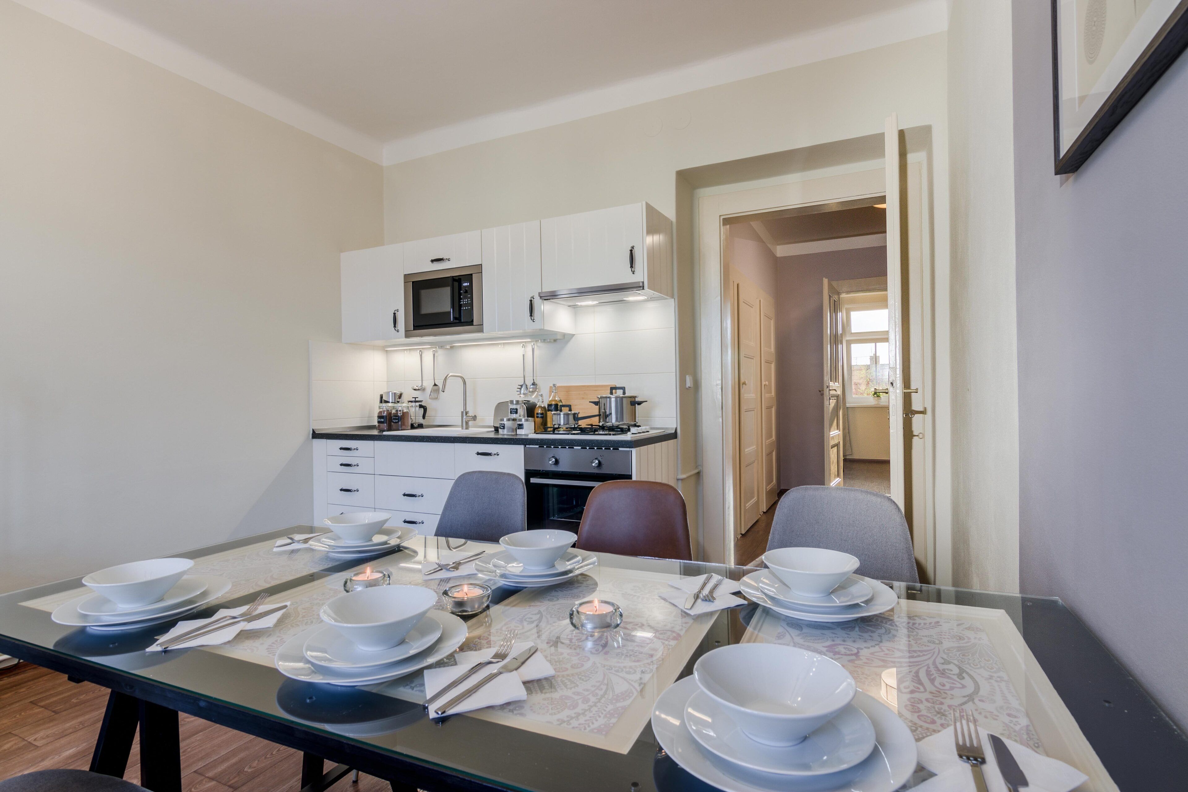Un comedor con una mesa preparada para cuatro, un microondas y una cocina al fondo.