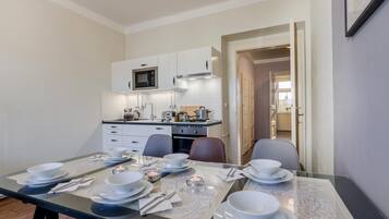 Un comedor con una mesa preparada para cuatro, un microondas y una cocina al fondo.