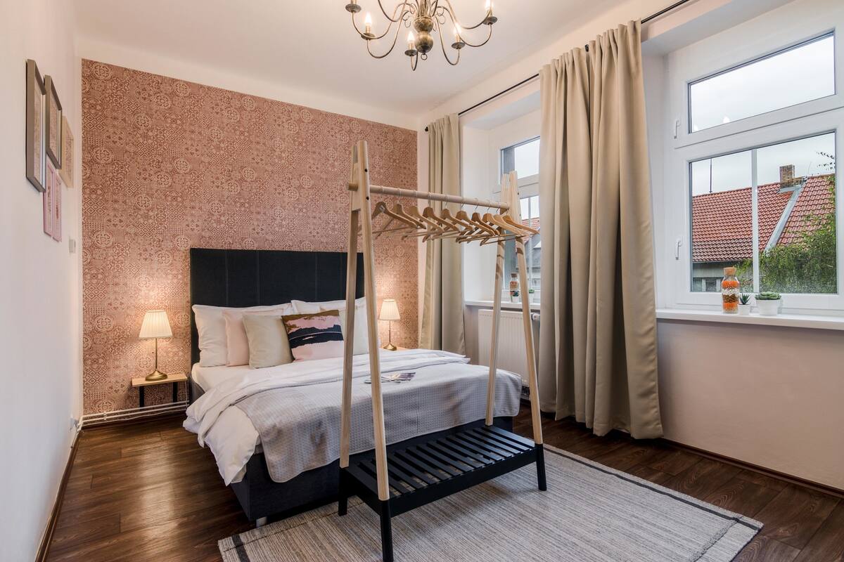 Een keurig opgemaakt slaapkamer met een bed, nachtlampjes, een kledingrek en een raam met gordijnen.