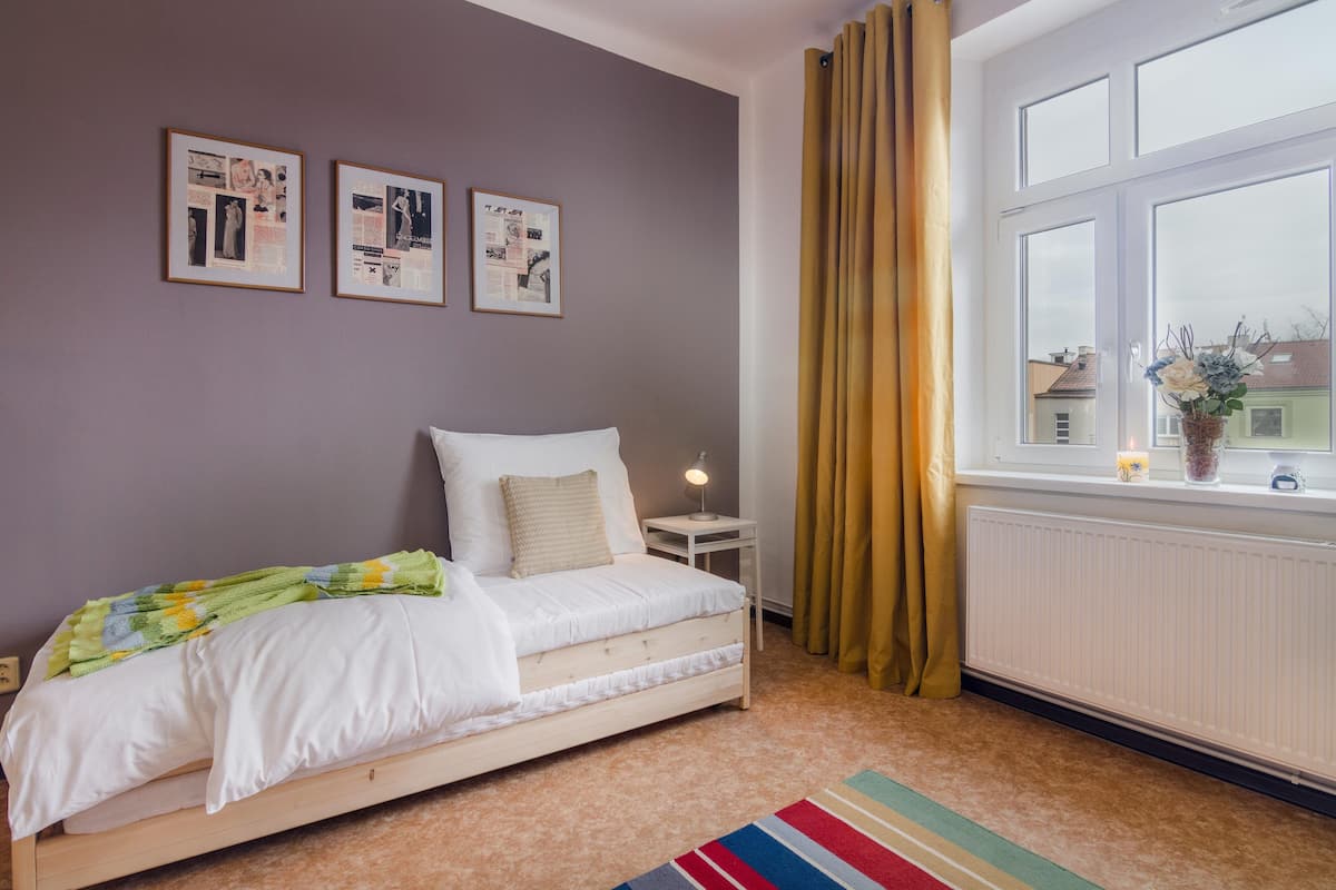 Een slaapkamer met een bed, een nachtkastje, een raam met gordijnen en wanddecoratie.