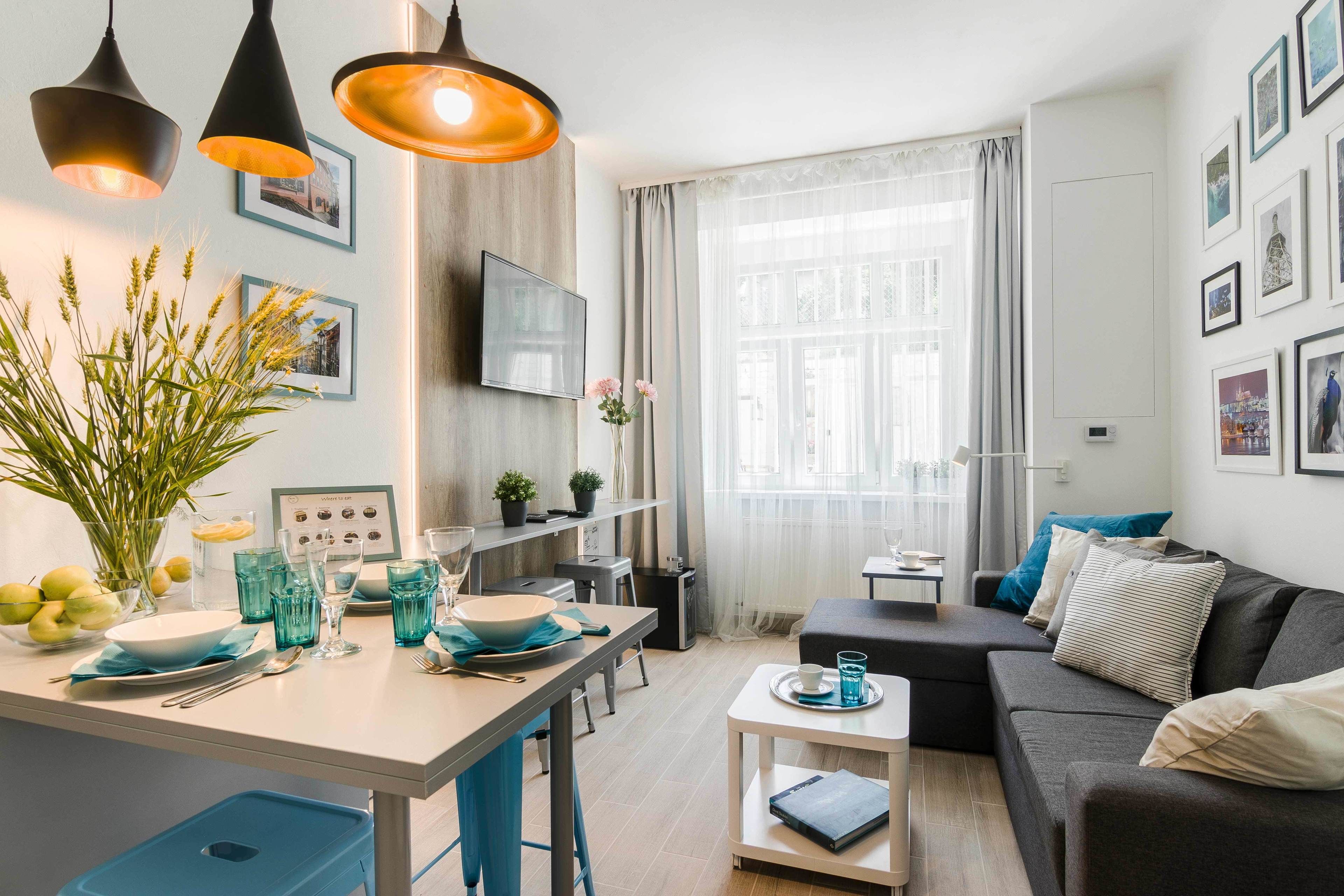 Un salon moderne comprenant un canapé, une table à manger avec des chaises bleues, un coin cuisine et une grande fenêtre avec des rideaux.