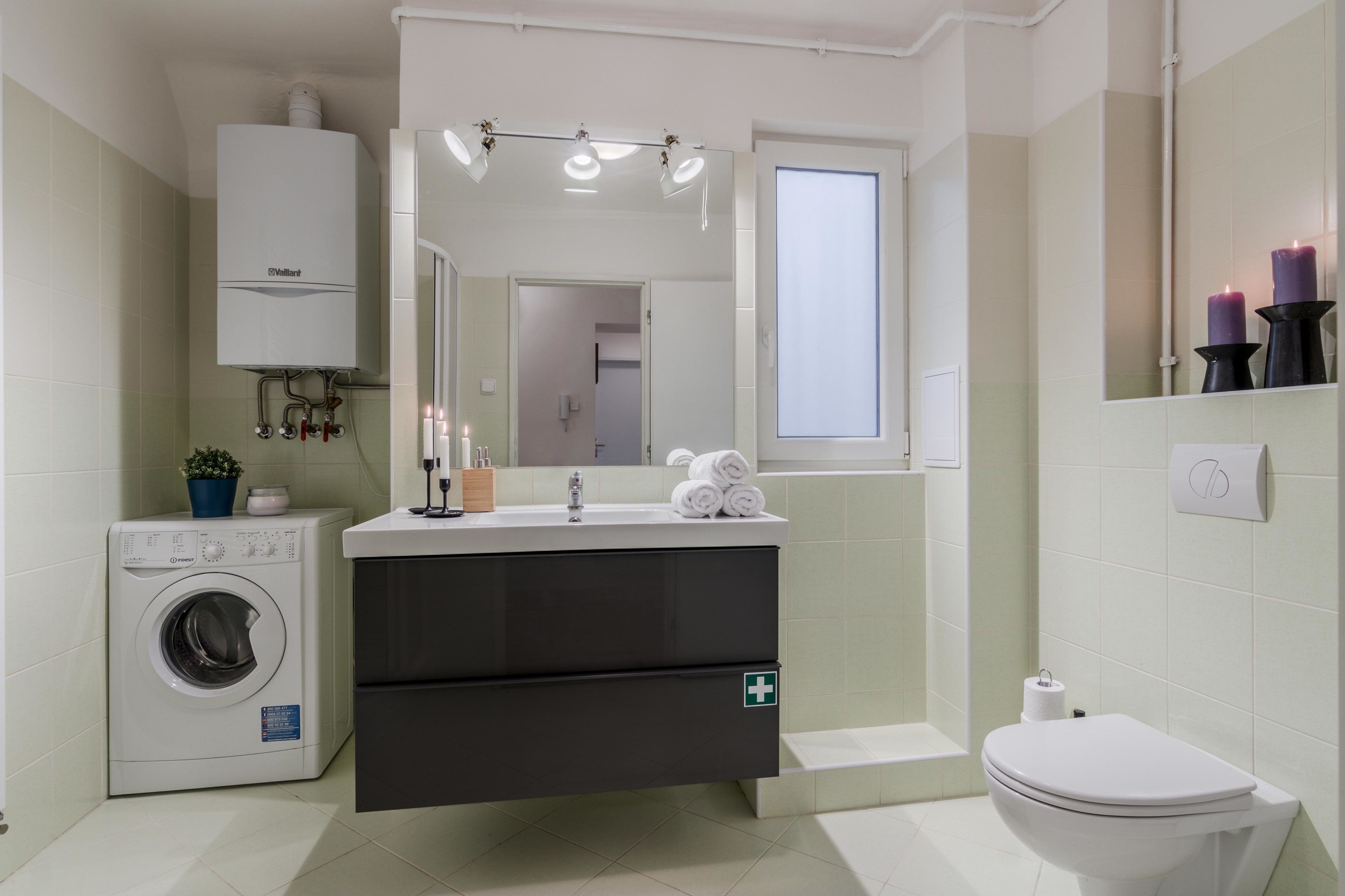 Un baño moderno con lavadora integrada, un lavabo con espejo arriba, inodoro y ventana.