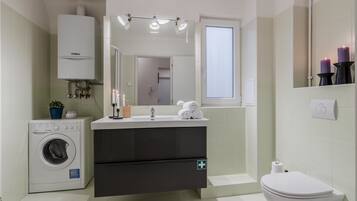 Un baño moderno con lavadora integrada, un lavabo con espejo arriba, inodoro y ventana.