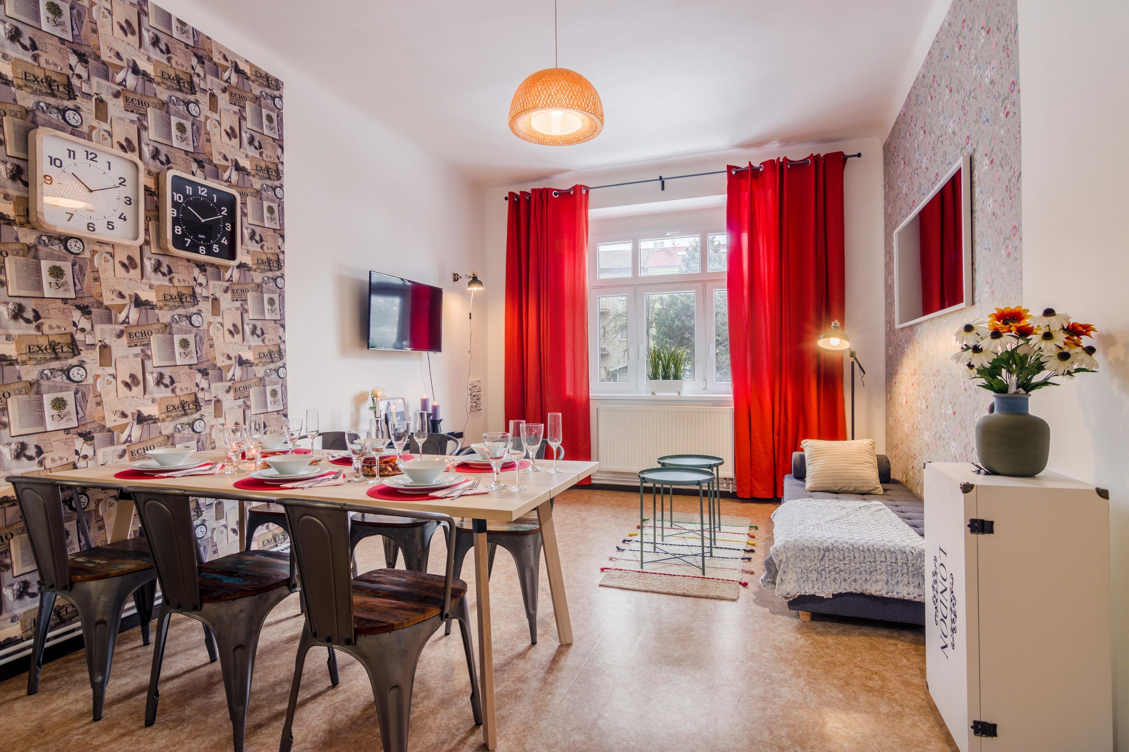 Un coin repas avec une table dressée pour quatre personnes, un canapé, un téléviseur et une fenêtre ornée de rideaux rouges.