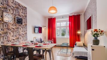 Un coin repas avec une table dressée pour quatre personnes, un canapé, un téléviseur et une fenêtre ornée de rideaux rouges.