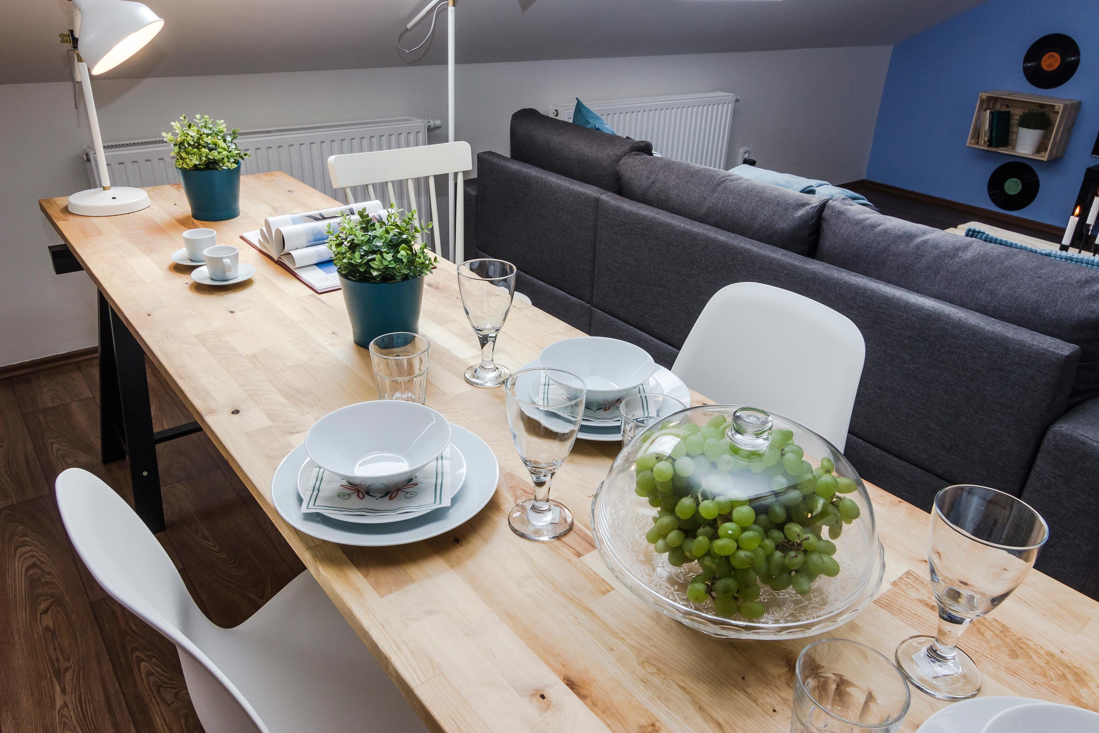 A dining area with a wooden table set for four, a grey sofa, and a blue wall with vinyl records.