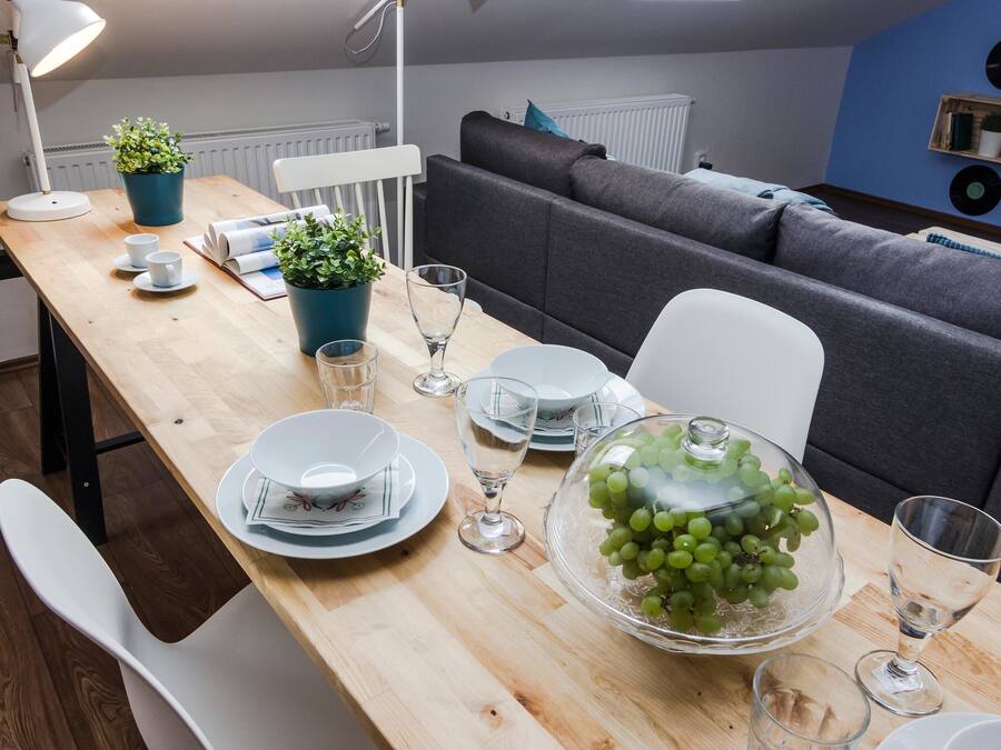 A dining area with a wooden table set for four, a grey sofa, and a blue wall with vinyl records.