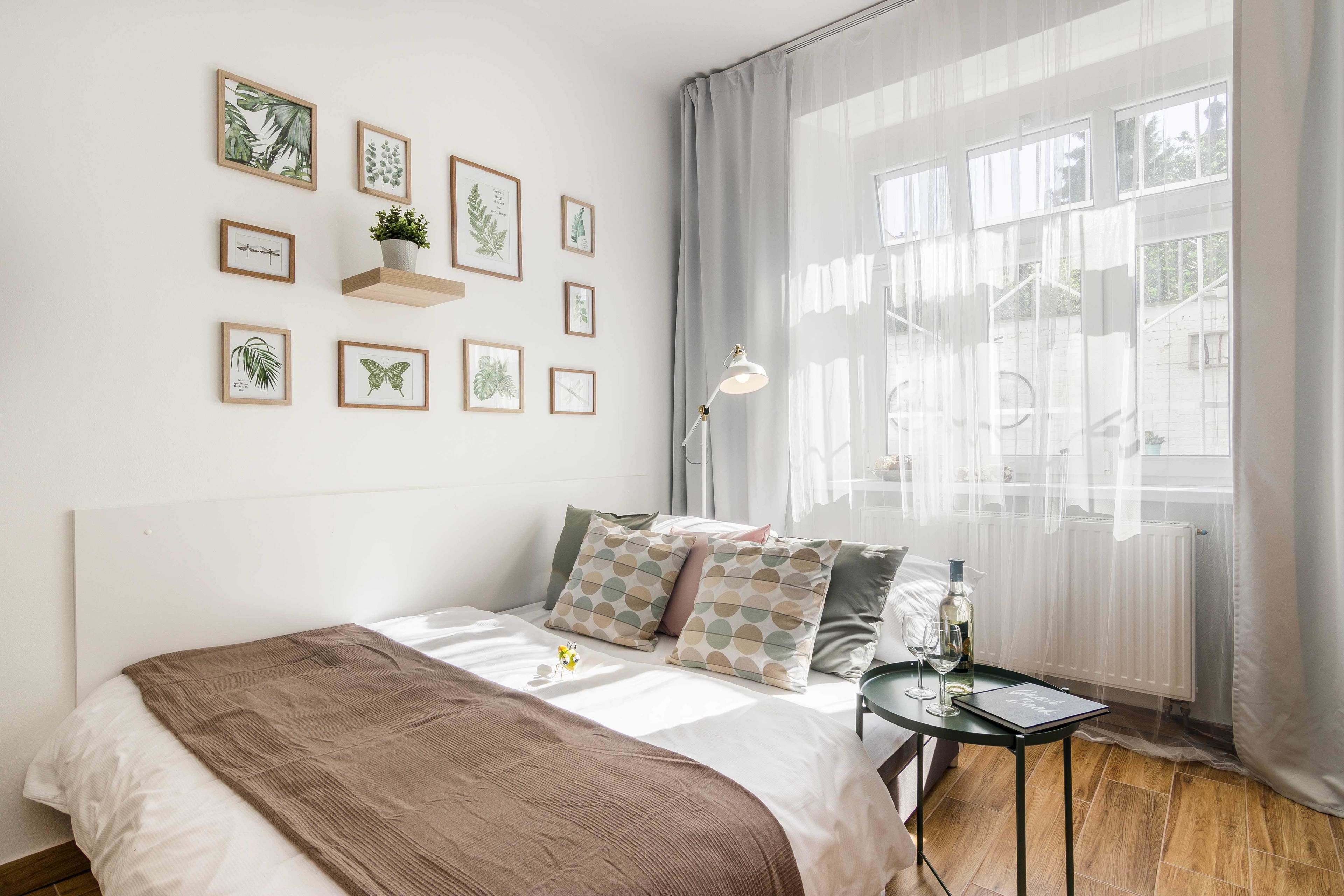 Une chambre à coucher bien rangée, avec un lit, des oreillers, une petite table avec une lampe et une fenêtre ornée de rideaux légers.