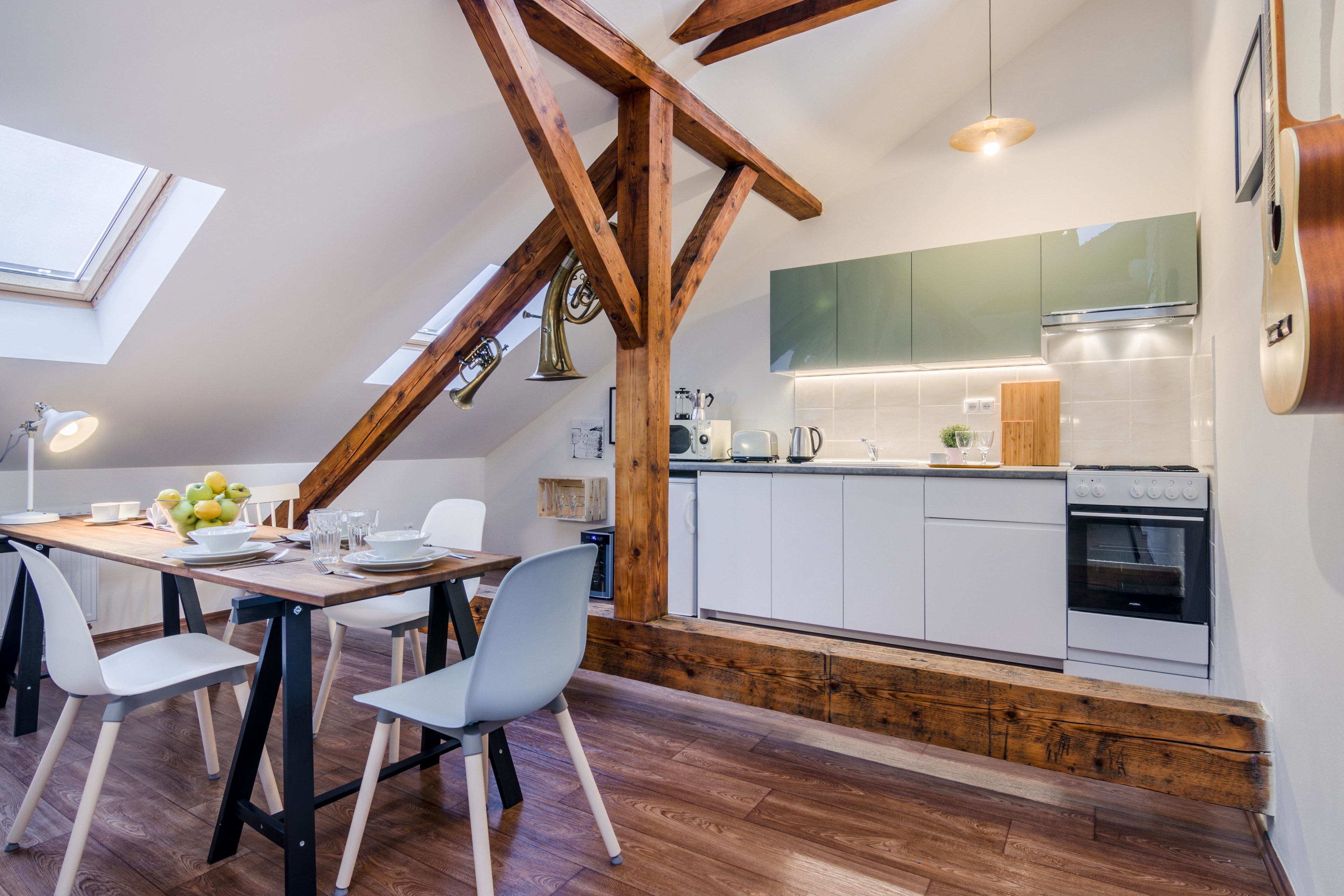 Una cucina moderna con mobili bianchi, forno integrato e travi in legno al soffitto.