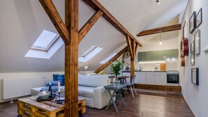 Eine Loft-Wohnung mit hohen Decken, Holzbalken, einer Essecke, einer Küche und einem Wohnbereich mit Sofa und Couchtisch.