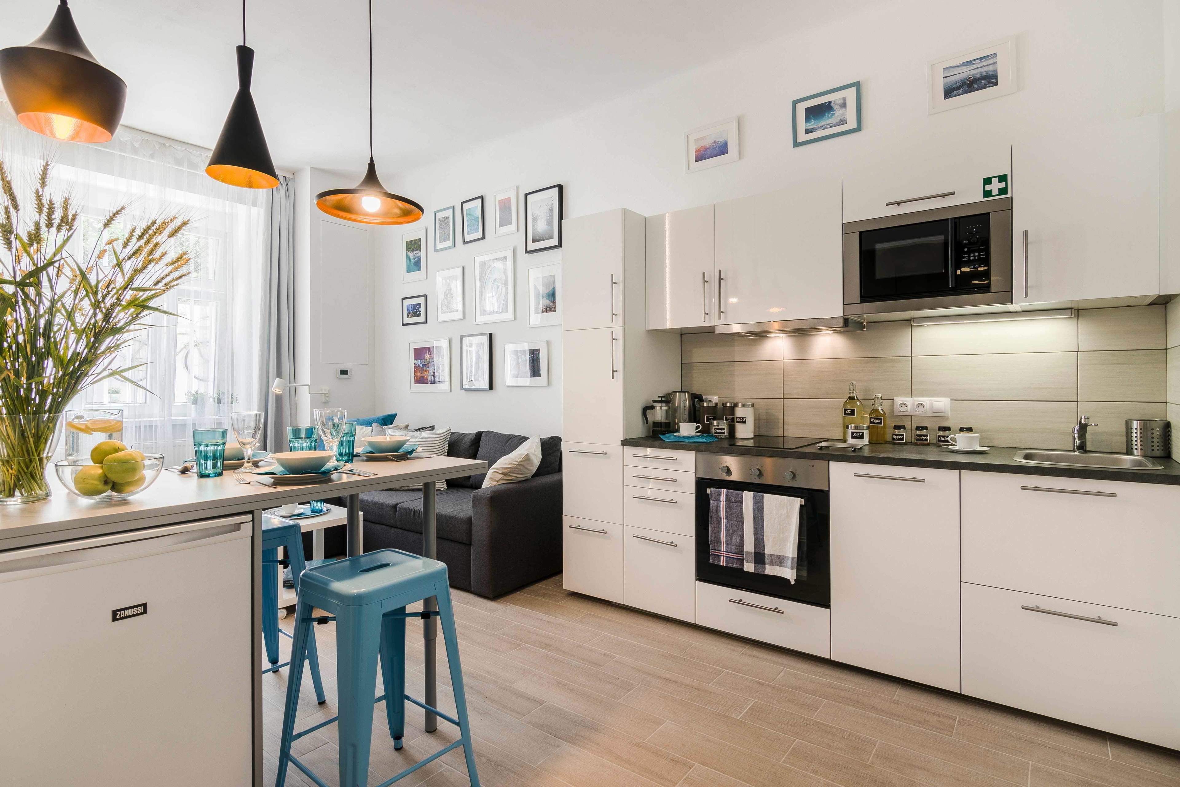 Une cuisine moderne avec des armoires blanches, un four à micro-ondes encastré et une cuisinière. On y trouve des tabourets de bar bleus et une table à manger avec des chaises.