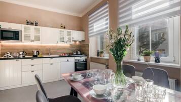 Une cuisine moderne avec des meubles blancs, une table à manger au plateau en verre et un vase rempli de fleurs.