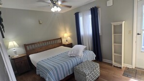 A bedroom with a bed, bedside lamps, a ceiling fan, a wardrobe, and a door. - Home Away From Home 2 (Hampton Beach)