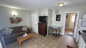 A living room with a sofa, coffee table, TV, and a dining area with a table and chairs. - Home Away From Home 2 (Hampton Beach)