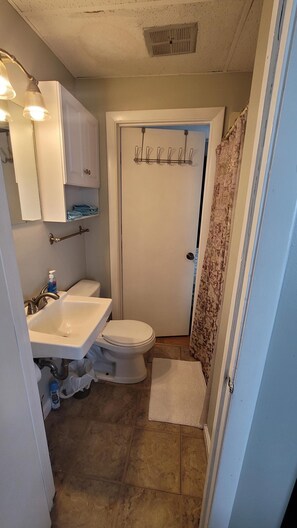 A compact bathroom with a white sink, toilet, and shower area. There is a towel rack above the shower door and a mirror above the sink. - Home Away From Home 2 (Hampton Beach)