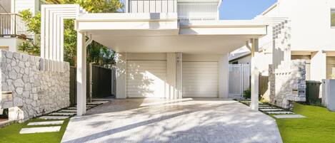 A modern house with a covered driveway, stone walls, and a well-maintained lawn.
