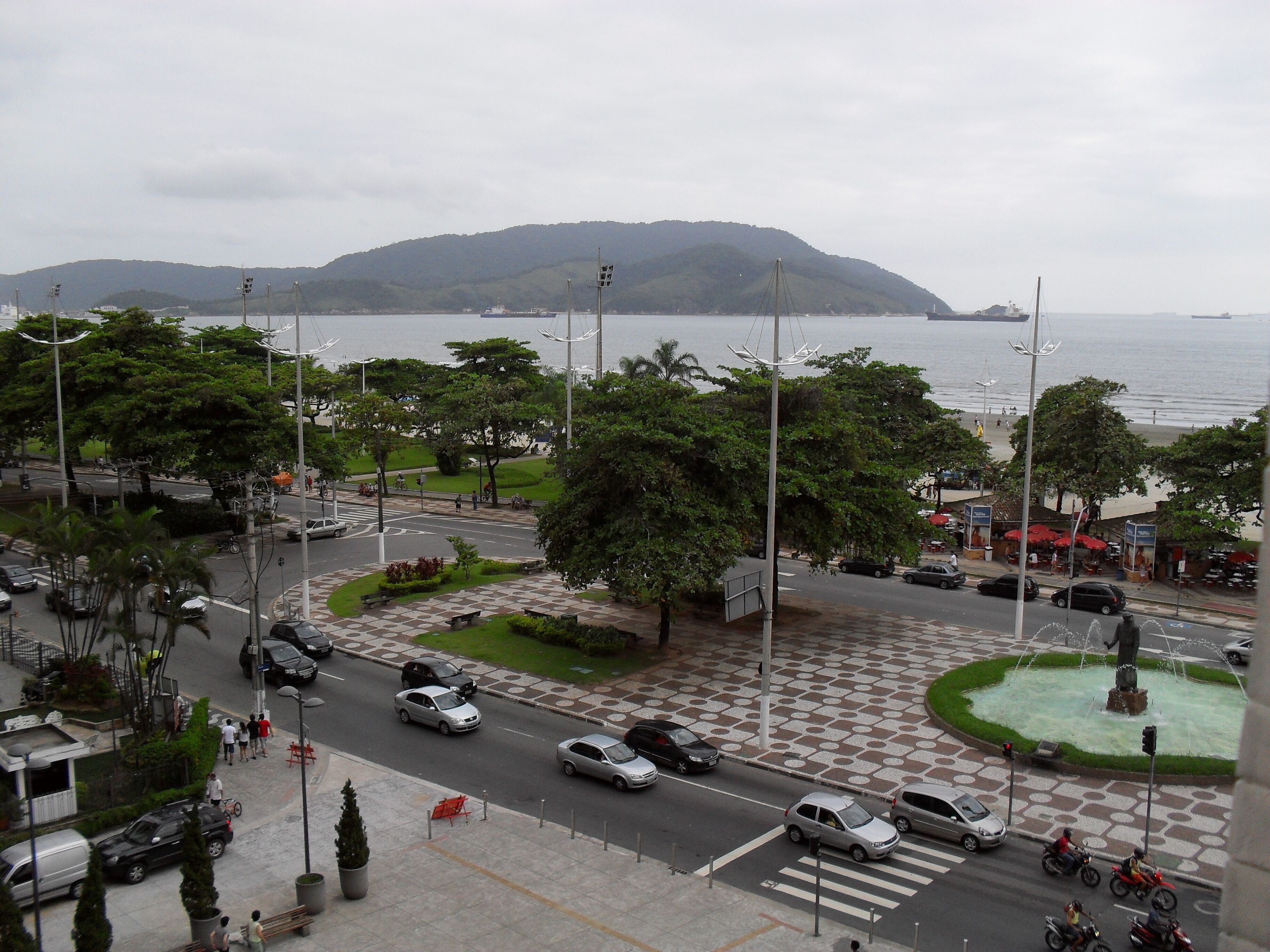 A cityscape with a roundabout, vehicles, and a distant view of the sea.