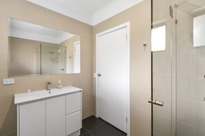 A bathroom with a white vanity, a mirror, and a glass-enclosed shower.