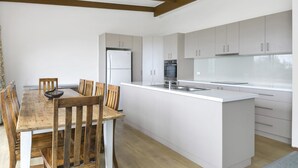 A modern kitchen with white cabinetry, a central island, and a dining area with wooden chairs and a table.