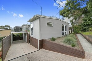 A single-story house with a covered patio, a small garden area, and a visible satellite dish. - On The Deck (Lorne)