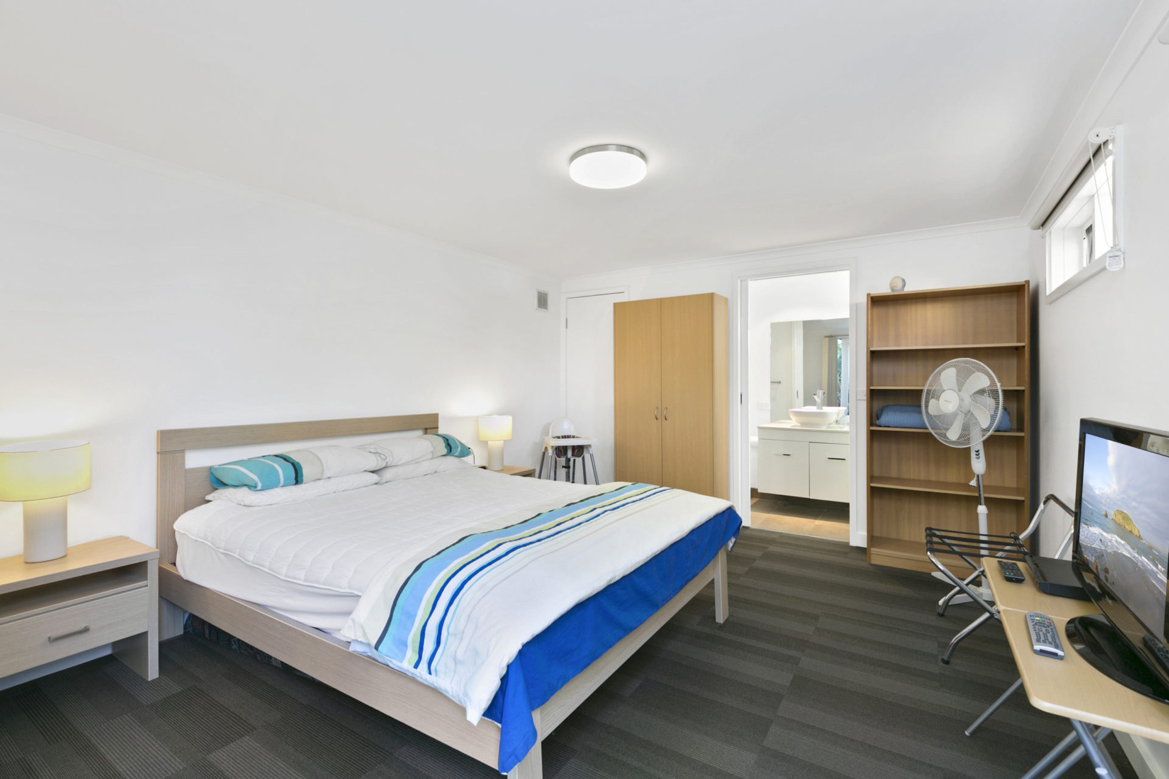 A hotel room with a bed, bedside tables, a desk with a chair, a TV, and a wardrobe.