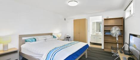A hotel room with a bed, bedside tables, a desk with a chair, a TV, and a wardrobe.