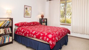 Un dormitorio con cama, estantería, mesita de noche, lámpara, ventana con cortinas y un cartel en la pared.
