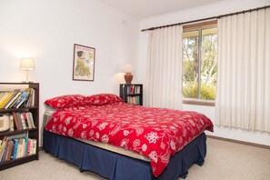 Ein Schlafzimmer mit einem Bett, einem Bücherregal, einem Nachttisch, einer Lampe, einem Fenster mit Vorhängen und einem Poster an der Wand.