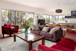 Ein geräumiges Wohnzimmer mit großem Fenster, einem roten Sofa, einem Holztisch und einem violetten Sofa mit dekorativen Kissen.