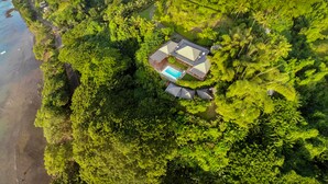 Oversigtsbillede af et resort med swimmingpool, omgivet af frodig vegetation og en strand.