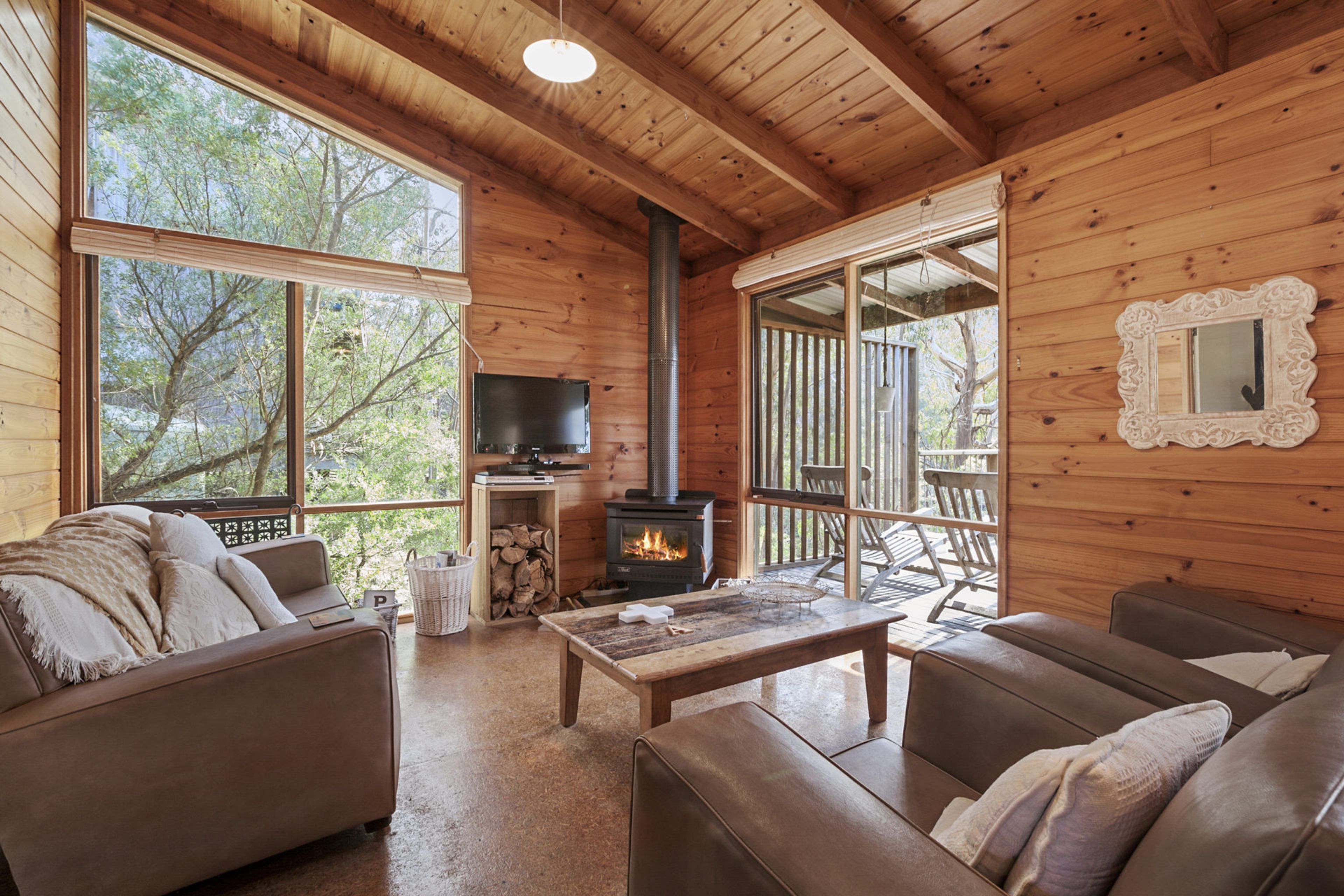 Un intérieur de chalet chaleureux avec une cheminée, des murs en bois et de grandes fenêtres.