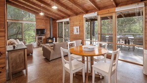 A wooden cabin with a dining area, a fireplace, and large windows.