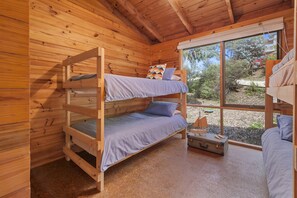 A wooden cabin with bunk beds, a small window, and a suitcase on the floor.