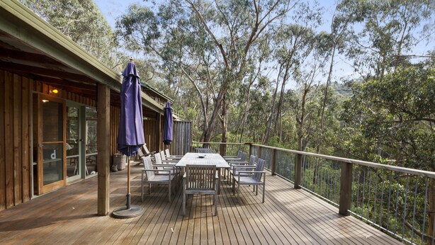 A wooden deck with a table and chairs, surrounded by trees.