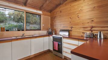 A kitchen with wooden walls, a window, a stove, and a sink.