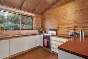 A kitchen with wooden walls, a window, a stove, and a sink.
