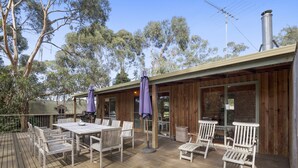An outdoor deck with a wooden table and chairs, surrounded by trees.