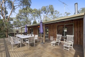 An outdoor deck with a wooden table and chairs, surrounded by trees.