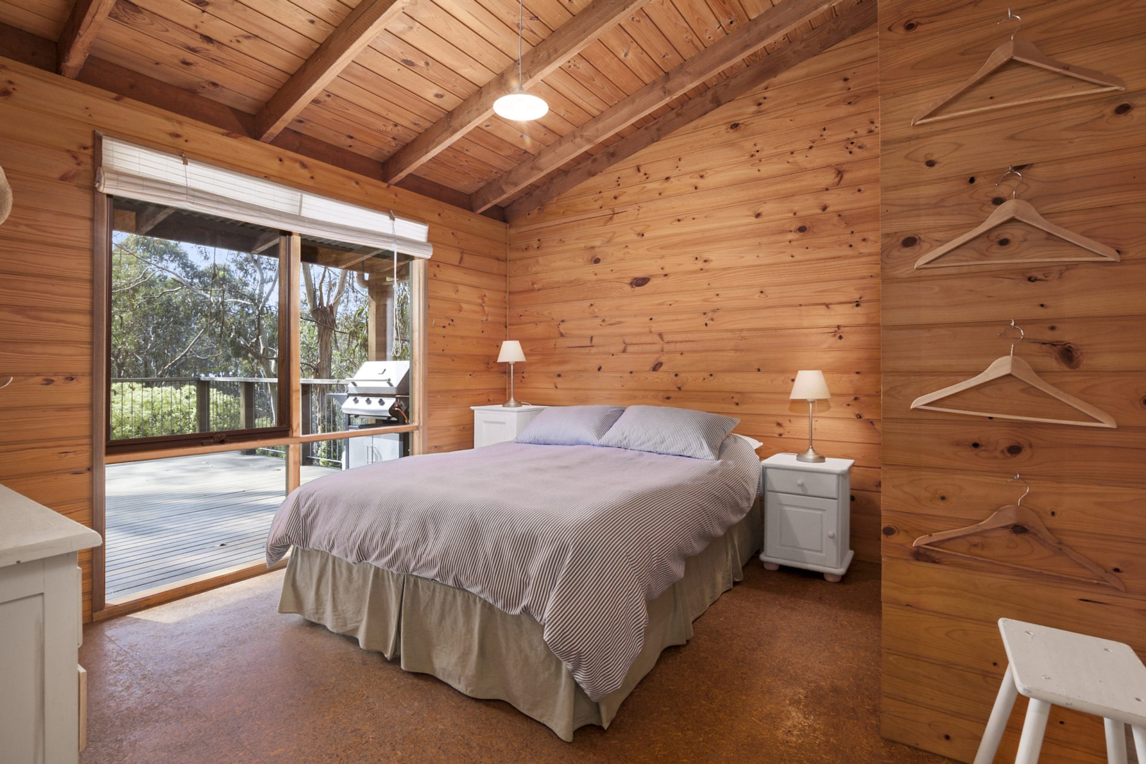A wooden cabin bedroom with a bed, bedside lamps, and a view of the outdoors.