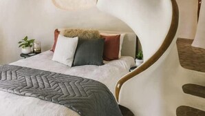 A uniquely designed bedroom with a curved headboard, a bed with multiple pillows, and a patterned throw blanket.