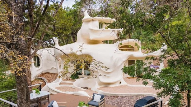A treehouse with a unique architectural design, surrounded by a patio area with outdoor furniture.