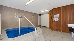A spa area with a blue pool, a wooden wall, and a sign indicating sauna hours.