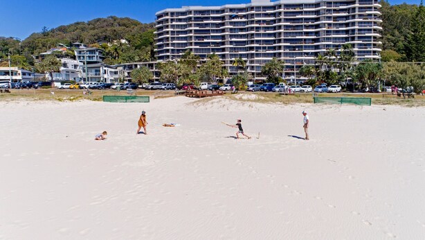 Une plage avec un grand bâtiment d’hôtel en arrière-plan, un terrain sablonneux et quelques personnes.